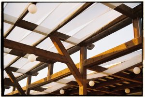 A detailed view of a rustic wooden pergola with white fabric and round light bulbs.