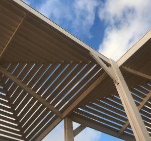 A low angle view of a wooden pergola with blue sky and white clouds in Haifa, Israel.