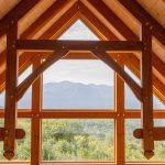 A rustic wooden interior featuring large windows framing a scenic mountain view.