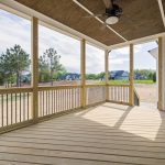 A bright wooden porch with ceiling fan and glass door, overlooking a grassy area.