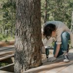 A man performs manual labor using a drill on a forest boardwalk construction project.